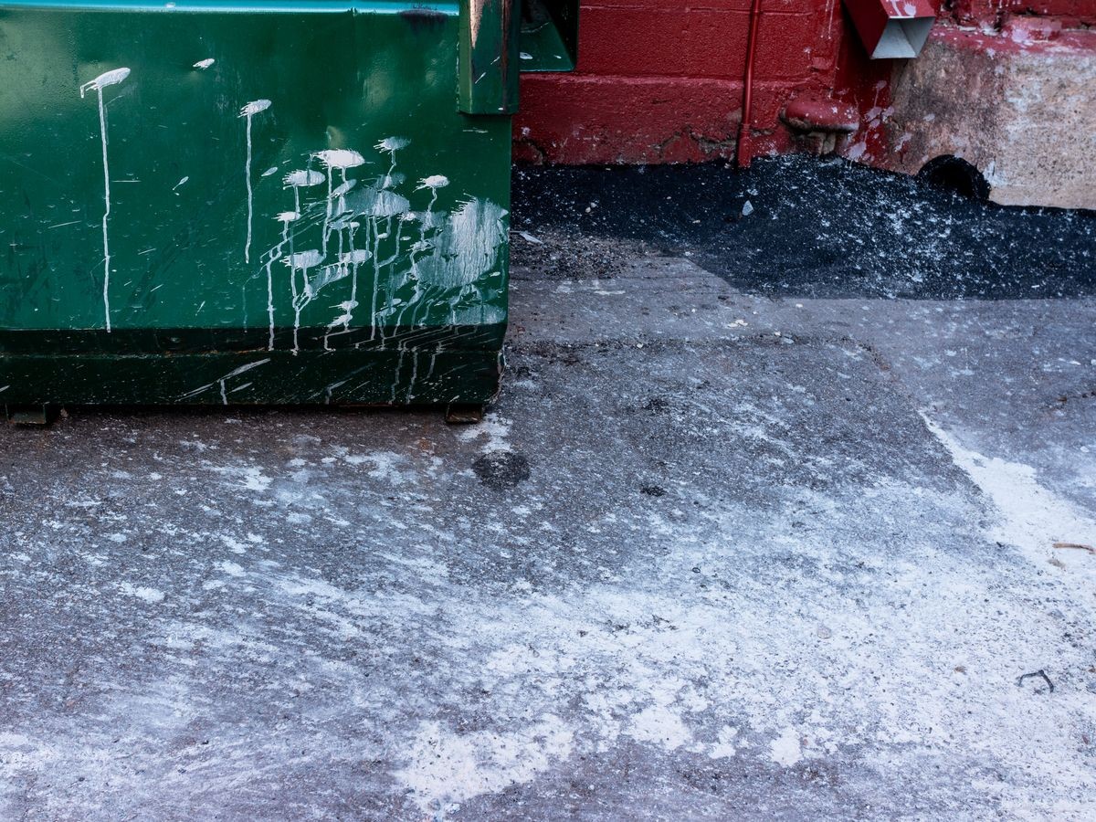 White paint splatter on asphalt and the corner of a green dumpster.