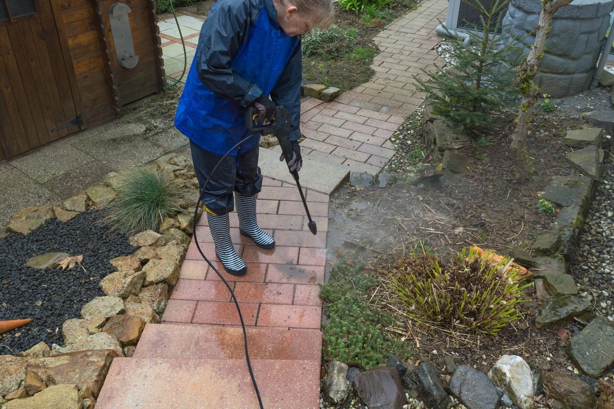 Woman cleans stone sidewalk with a pressure washer